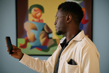 African American male in white shirt looking at a smartphone, colorful abstract art in background creating a visually engaging scene