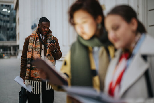 Scene of three individuals in professional attire engaged in their respective tasks outside an office building, portraying dedication, focus, and teamwork in a city setting during the day.