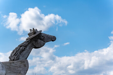 An imaginative wooden sculpture in the shape of a horse with a hat towers against a light blue sky. The childlike, playful design is both charming and artistic.
