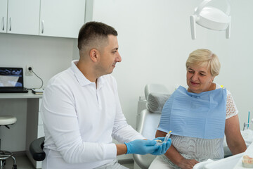 Obraz premium dentist consulting a retired woman with the installation of a tooth crown, an implant. Artificial teeth with steel pin