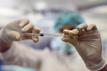 nurse wear white coat maask, hat and gloves preparing to inject medicine to treat a patient