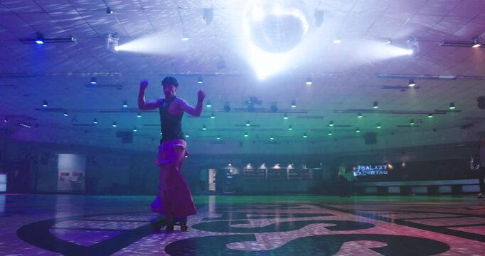 Foggy dance floor with guy roller blading beneath disco ball by himself - wide, low shot