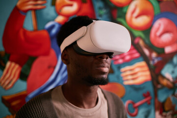 African American man immersed in virtual reality using advanced VR headset indoors surrounded by...