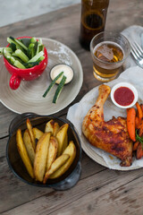 Top-down view of pub food: baked chicken drumsticks, rustic fries, sliced pickles, sauces, and beer. Cozy and casual atmosphere. Perfect for menus, blogs, or food delivery visuals