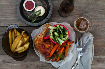 Top-down view of pub food: baked chicken drumsticks, rustic fries, sliced pickles, sauces, and beer. Cozy and casual atmosphere. Perfect for menus, blogs, or food delivery visuals