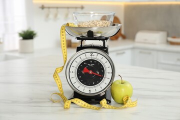 Kitchen scales with oatmeal, measuring tape and apple on light marble table indoors