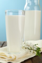 Fresh milk and blossoms on wooden table against light blue background, closeup