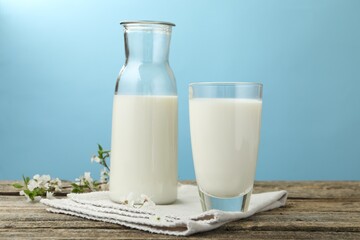 Fresh milk and blossoms on wooden table against light blue background, closeup