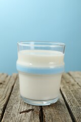 Fresh milk in glass on wooden table against light blue background, closeup
