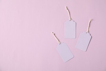 Blank tags with strings on pale violet background, flat lay. Space for text