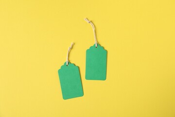 Blank tags with strings on yellow background, flat lay