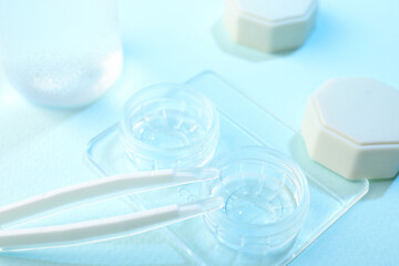 Case with contact lenses and tweezers on light blue background, closeup