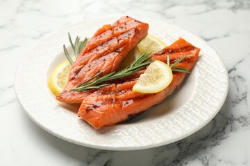 Seafood. Tasty grilled salmon served with rosemary and lemon on white marble table, closeup