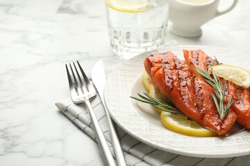 Seafood. Tasty grilled salmon served with cutlery, rosemary and lemon on white marble table, closeup. Space for text