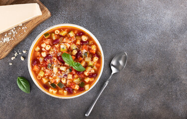Minestrone soup with fresh vegetables, beans, pasta, parmesan cheese and basil on a gray background. Italian cuisine.