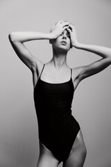 Fototapeta premium Elegant model in black swimsuit posing dramatically against a soft gray background, conveying emotions of strength and vulnerability in a fashion concept.