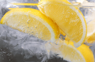 Refreshing soda water with slices of lemon and ice in glass on dark background, closeup