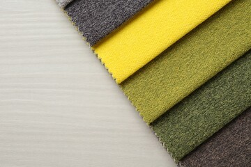 Samples of different fabrics on light wooden table, top view. Space for text
