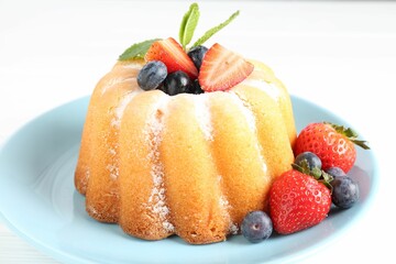 Tasty Bundt cake with powdered sugar and berries on white table, closeup