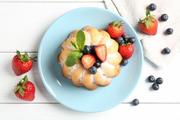 Tasty Bundt cake with powdered sugar and berries on white wooden table, flat lay