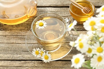Delicious chamomile tea in glass cup, fresh flowers, honey and teapot on wooden table, above view