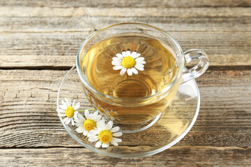 Delicious chamomile tea in glass cup and fresh flowers on wooden table, above view