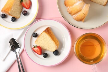 Pieces of tasty bundt cake with berries and tea on pink wooden table, flat lay