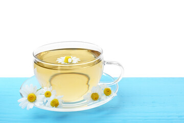 Delicious chamomile tea in glass cup and fresh flowers on light blue wooden table against white background