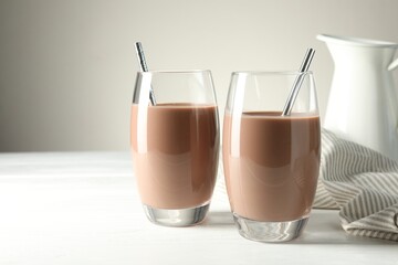 Tasty chocolate milk in glasses on white wooden table, space for text