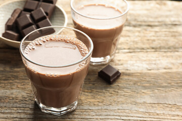 Tasty chocolate milk in glasses and pieces on wooden table, closeup. Space for text