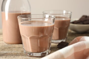 Tasty chocolate milk in glasses and pieces on wooden table, closeup