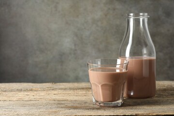 Tasty chocolate milk in glass and bottle on wooden table, space for text