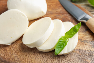 Cut mozzarella cheese with basil and knife on wooden table, closeup