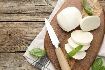Cut mozzarella cheese with basil and knife on wooden table, flat lay. Space for text