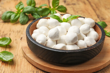 Mozzarella cheese balls and basil on wooden table, closeup