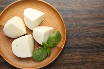 Pieces of delicious mozzarella cheese and basil on wooden table, top view. Space for text