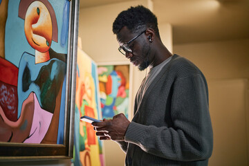 Man engaged in examining contemporary paintings in an art gallery space. He is deep in thought, focused on his surroundings and the artwork being observed