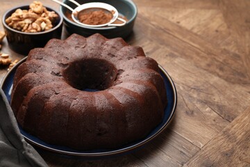 Tasty chocolate bundt cake, walnuts and cocoa powder on wooden table, closeup. Space for text