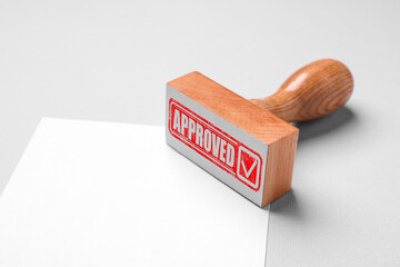Wooden stamp with word Approved and blank sheet of paper on table
