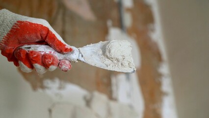 Construction worker applying plaster on damaged wall using putty knife