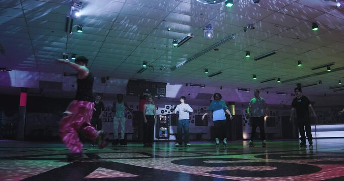 Roller skater doing epic spins and dance tricks in front of friends with disco lights - low, wide, steady cam shot