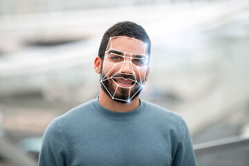 A man stands smiling outdoors while facial recognition technology analyzes his features. This...