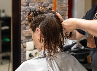Fototapeta premium Hair stylist cutting wet hair of customer in a professional salon environment