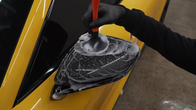 Detailing procedure of applying a soapy solution to the car's mirror using a brush 4k video. Meticulous car detailing at the carwash.