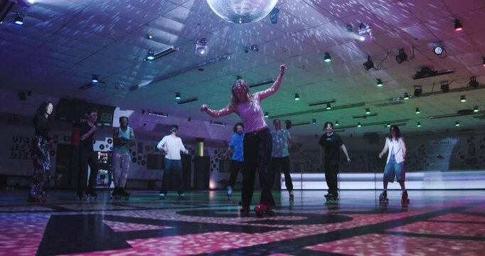 Young roller skater dancing in front of friends under disco ball on skate floor, epic steady cam movement