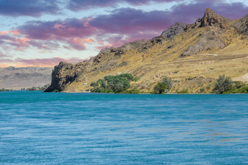 Naklejka premium Enjoy the beauty of nature in all its glory. Watch the sun set over the calm river. Enjoy the majestic mountains and lush green trees surrounding you.