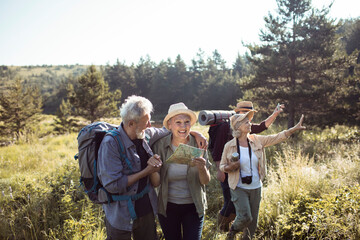 Group of senior friends hiking through forest trail with backpacks and map on a sunny day
