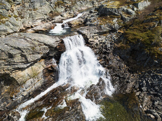 Powerful cascading waterfall among rocky mountains of Norway, crystal clear water, and wild northern nature on a summer day.