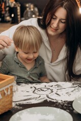 Mother and toddler smiling while drawing a sun in flour on the table during a cozy kitchen moment filled with love, messy play, warmth, and gentle parenting in a natural home setting