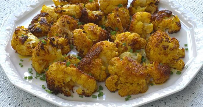 Roasted cauliflower with turmeric on a serving plate. Great vegan snack. Table spin.